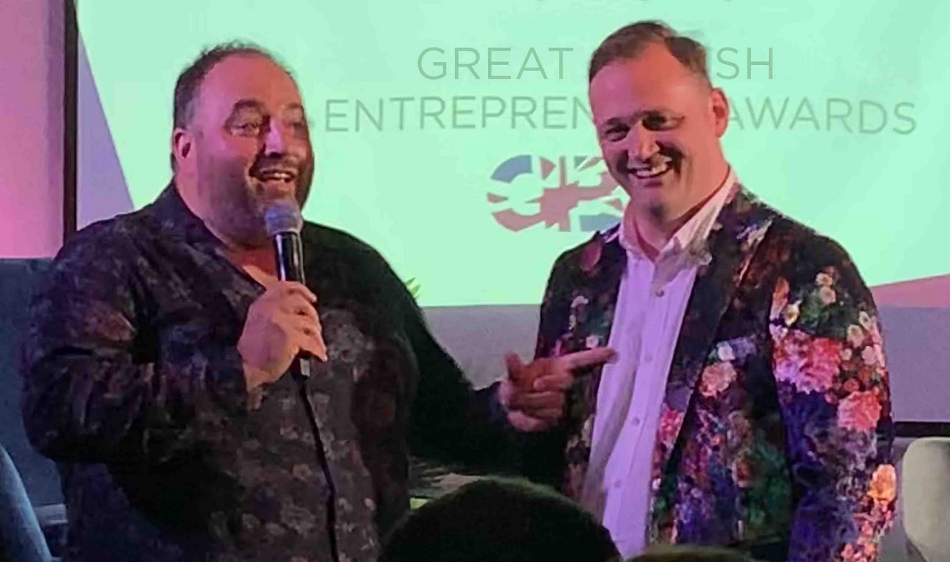 Welsh opera singer Wynne Evans and popcorn founder Simon Washbrook, in a floral jacket, speaking at a Great British Entrepreneur Awards event